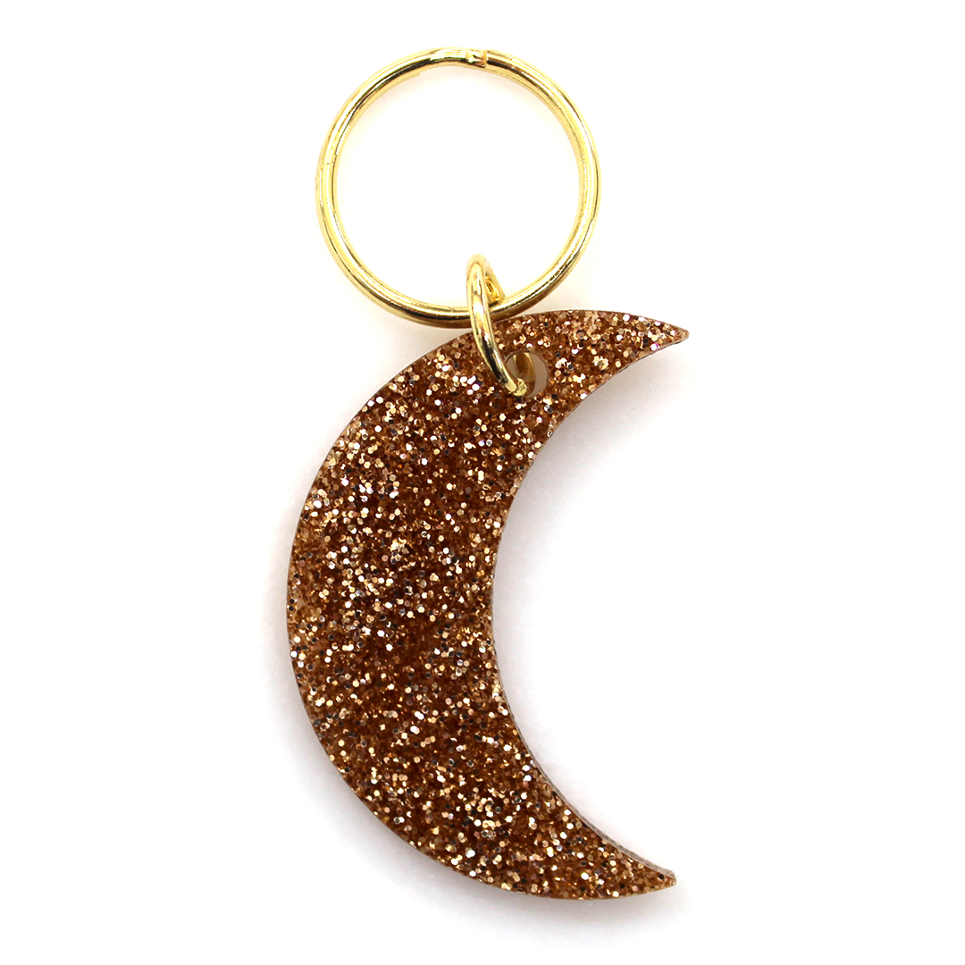 A gold glitter crescent moon keychain with a gold ring on a white background.