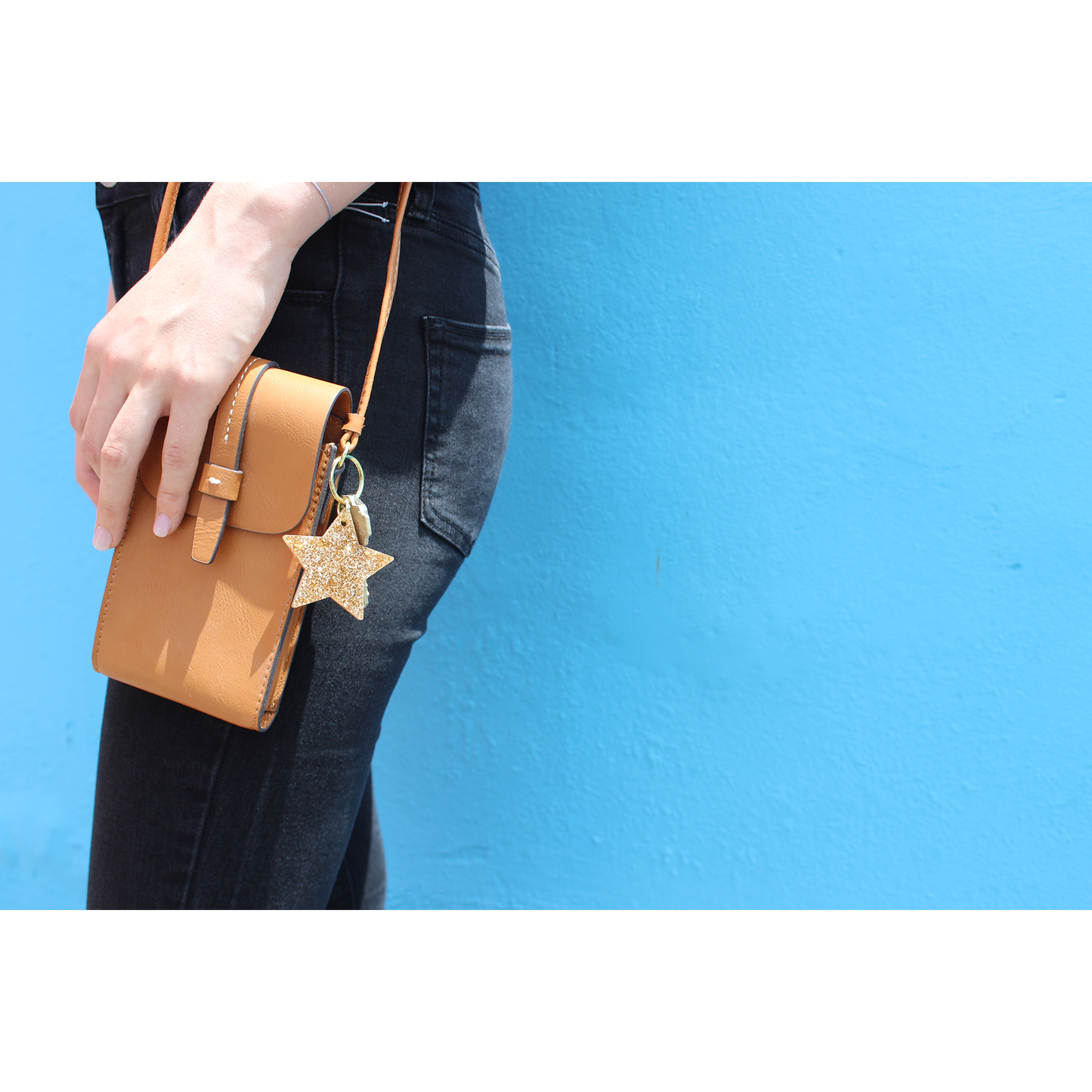 Person wearing black jeans with a brown purse and gold star keychain against a blue wall.