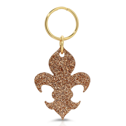 A gold key ring with a glittery fleur-de-lis charm hangs on a white background.