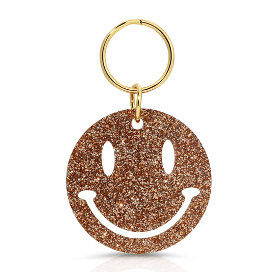 A glittery gold smiley face keyring on a white background.
