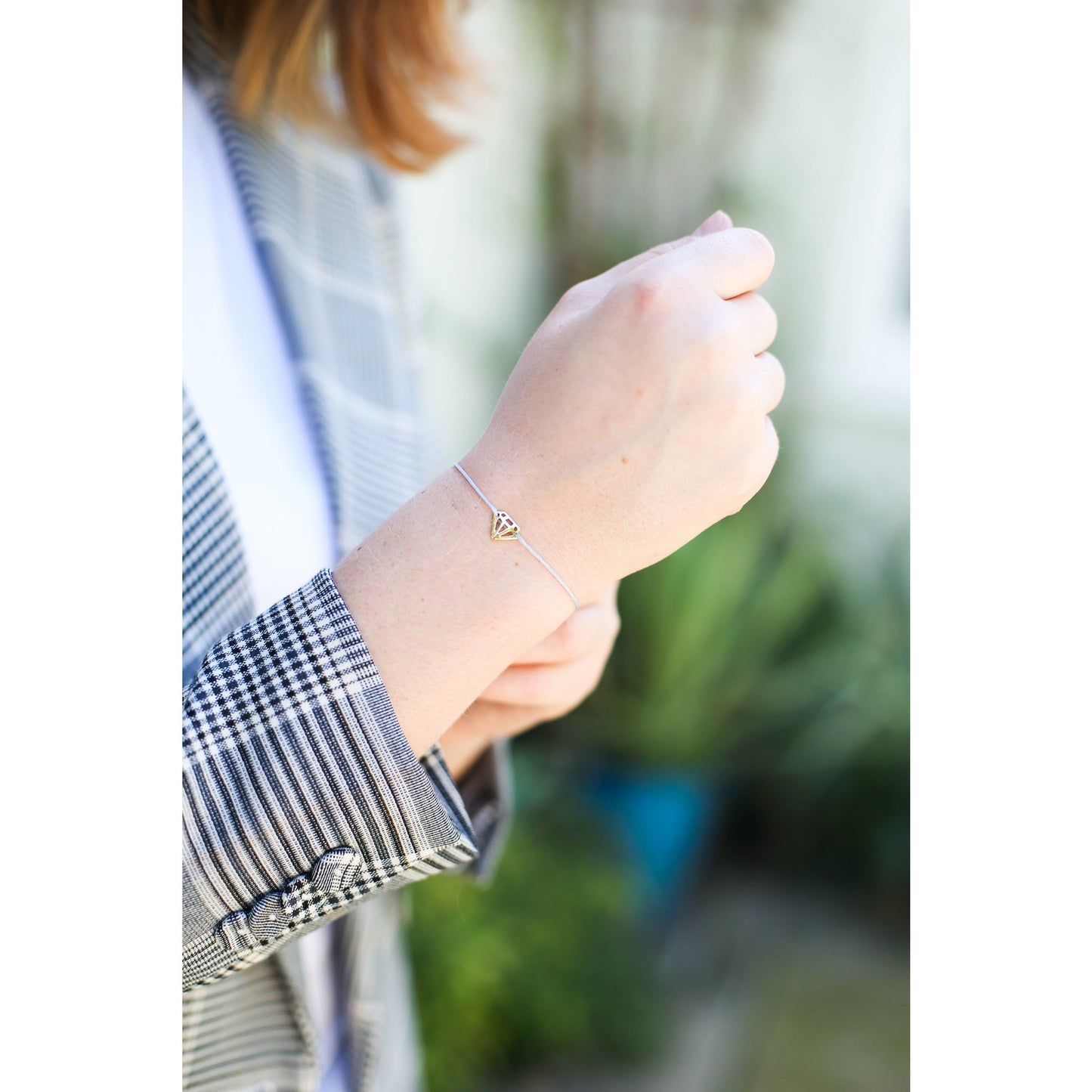 A person wears a thin bracelet with a diamond-shaped charm.