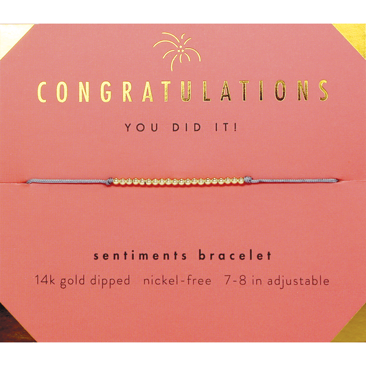 A gold beaded bracelet rests on a pink congratulations card.