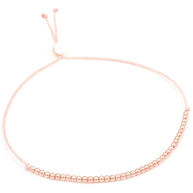A pale pink string bracelet with small rose gold-colored beads along part of the strand is displayed.