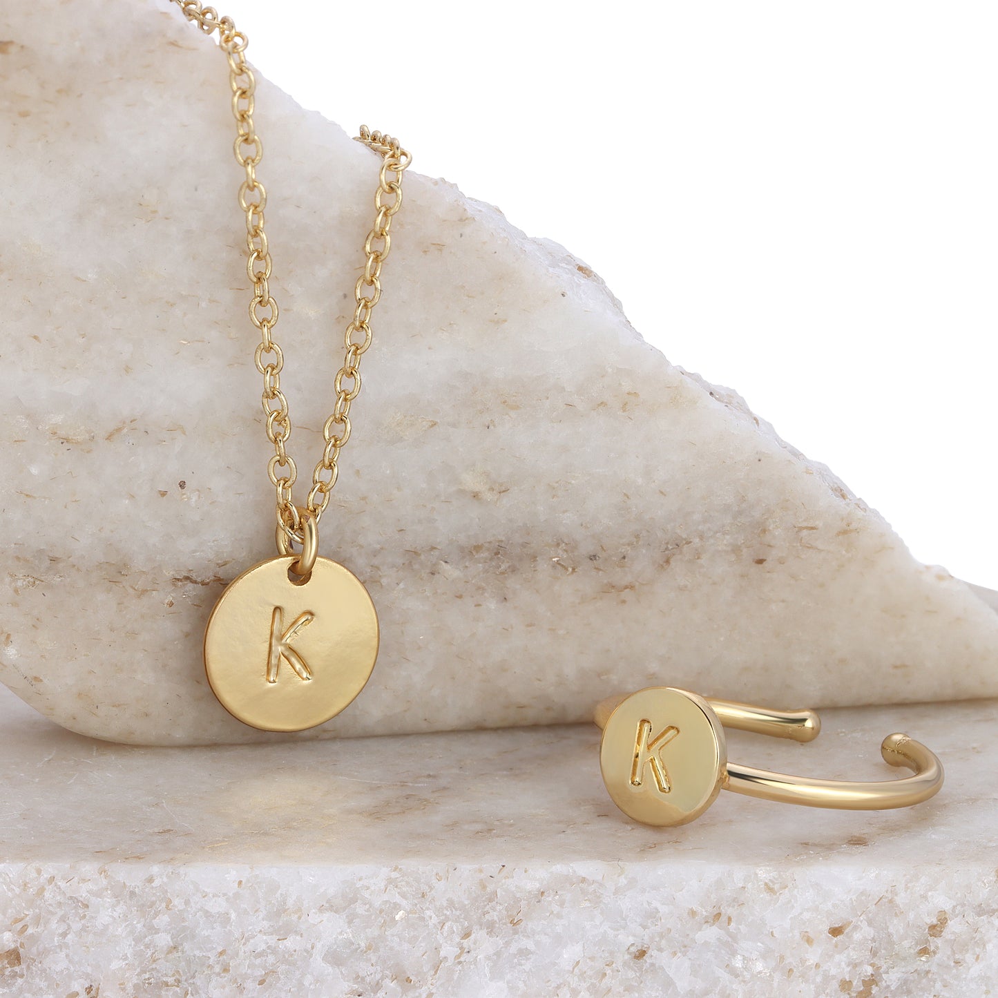 Gold necklace and ring with the letter K on a marble surface.