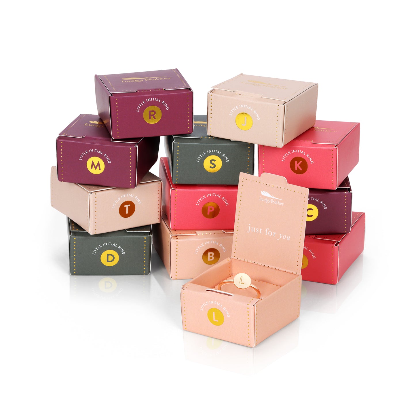 A stack of colorful gift boxes with the phrase "Little Initial Ring" and a letter on each, with one box open to reveal a gold ring.