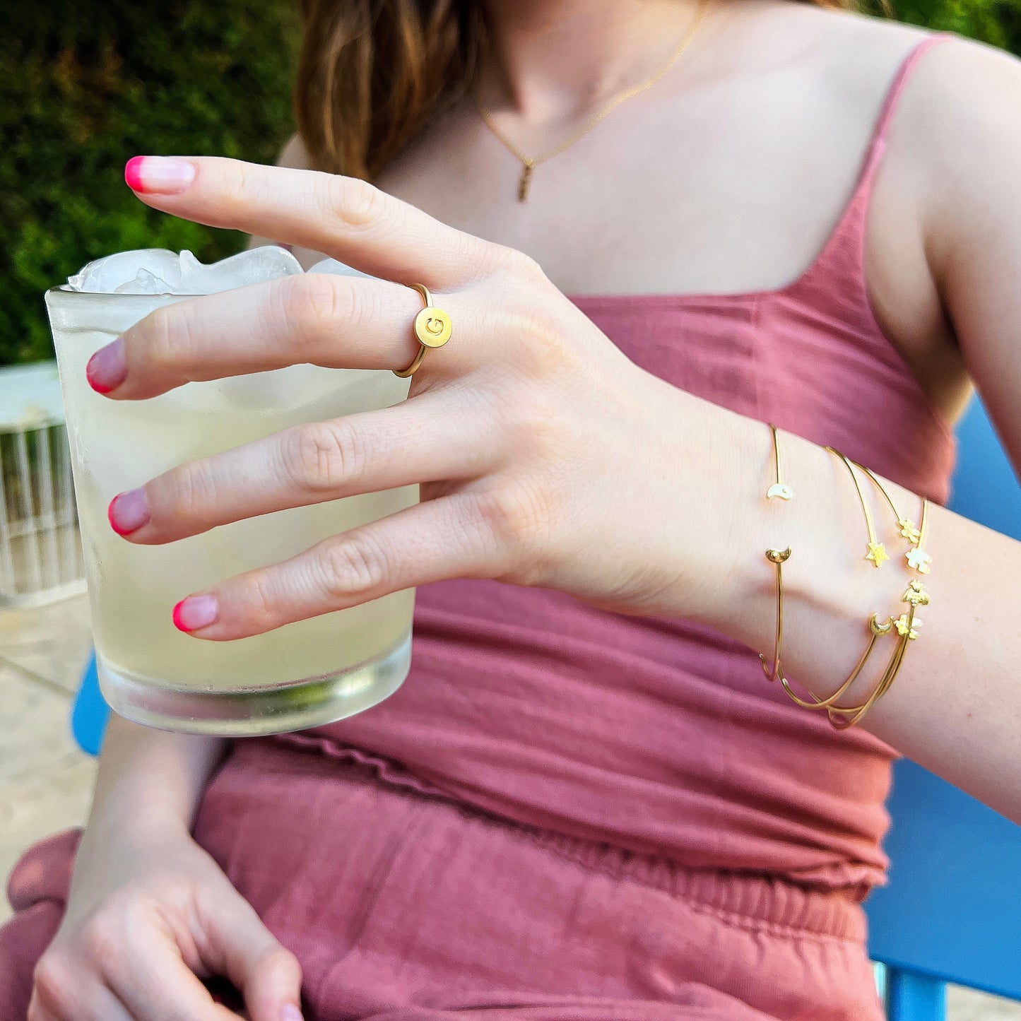 A woman holding a glass of iced beverage wears gold jewelry.
