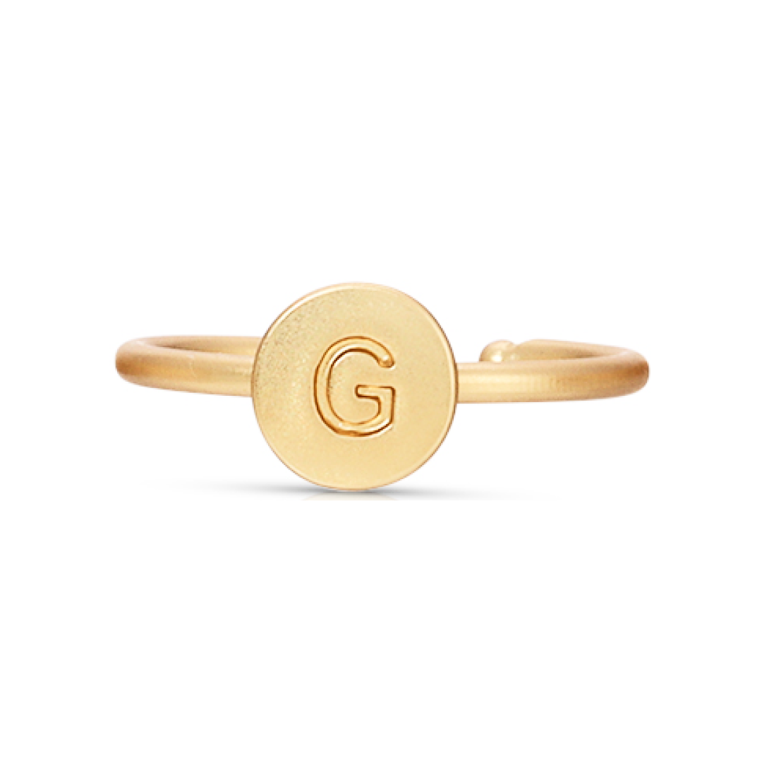 A gold ring features a circular plate with the letter "G" embossed on it.