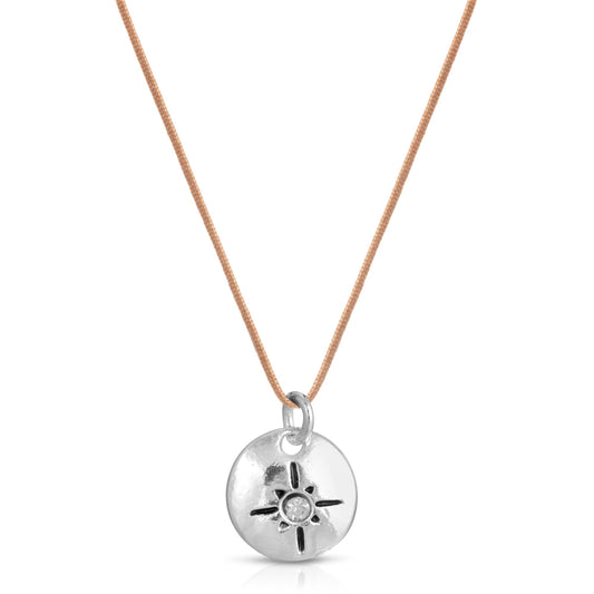 A necklace with a silver disc pendant featuring a sun or starburst design on a tan cord.