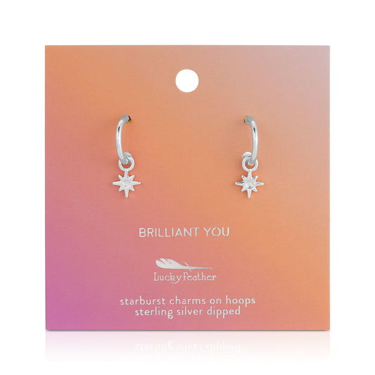 A pair of sterling silver dipped hoop earrings with starburst charms on a 'Brilliant You' Lucky Feather display card.