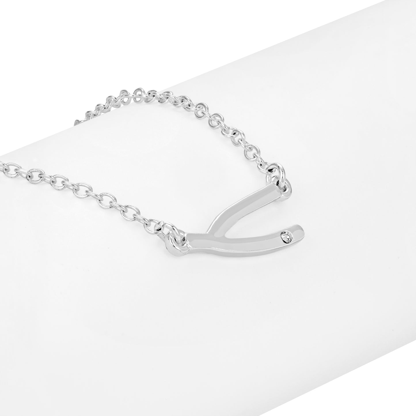 A silver wishbone pendant necklace with a small stone on a white cylindrical surface.