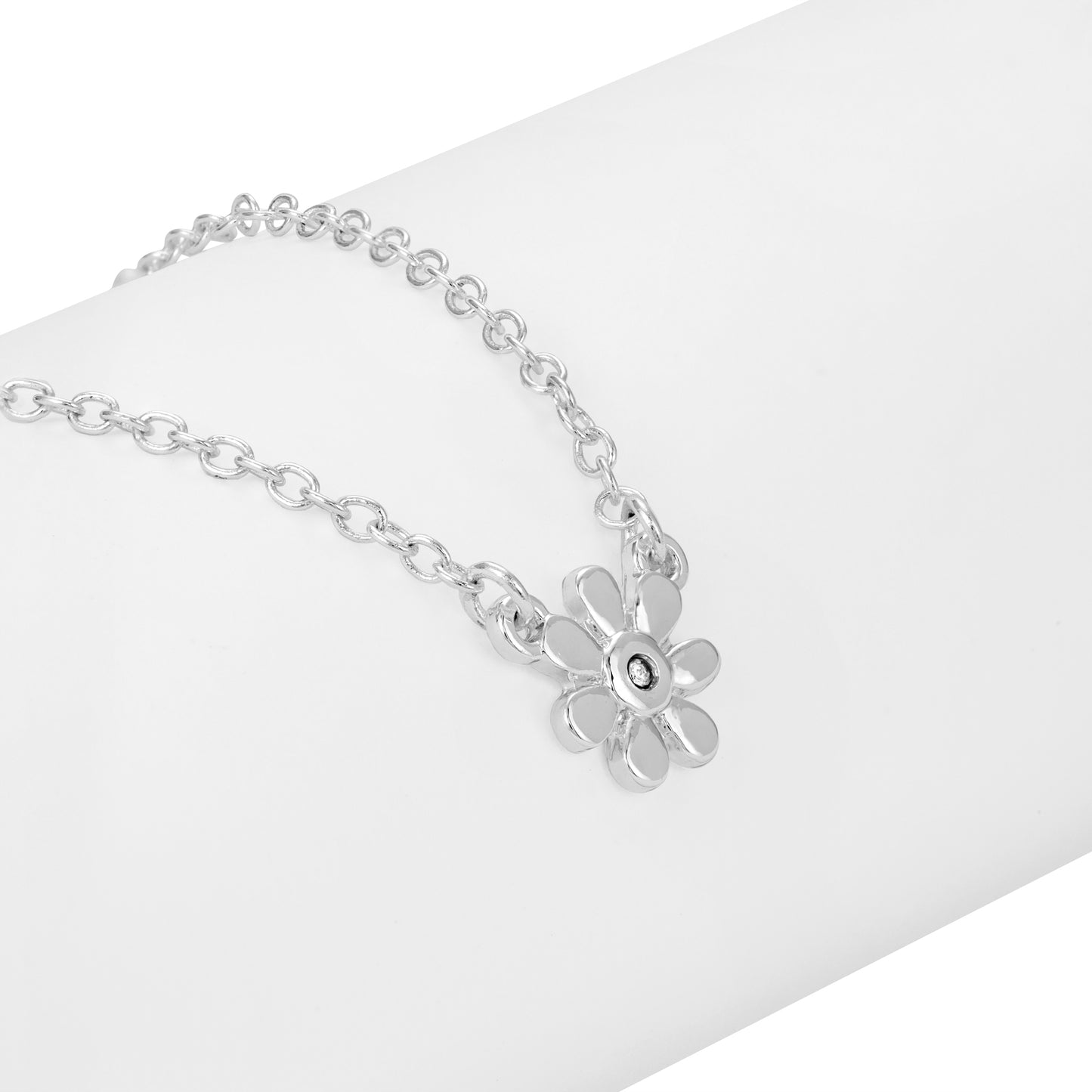 A silver-toned chain necklace with a flower pendant lies on a white surface.