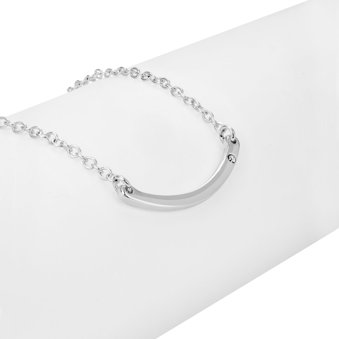 A silver necklace with a curved bar pendant lies on a white surface.