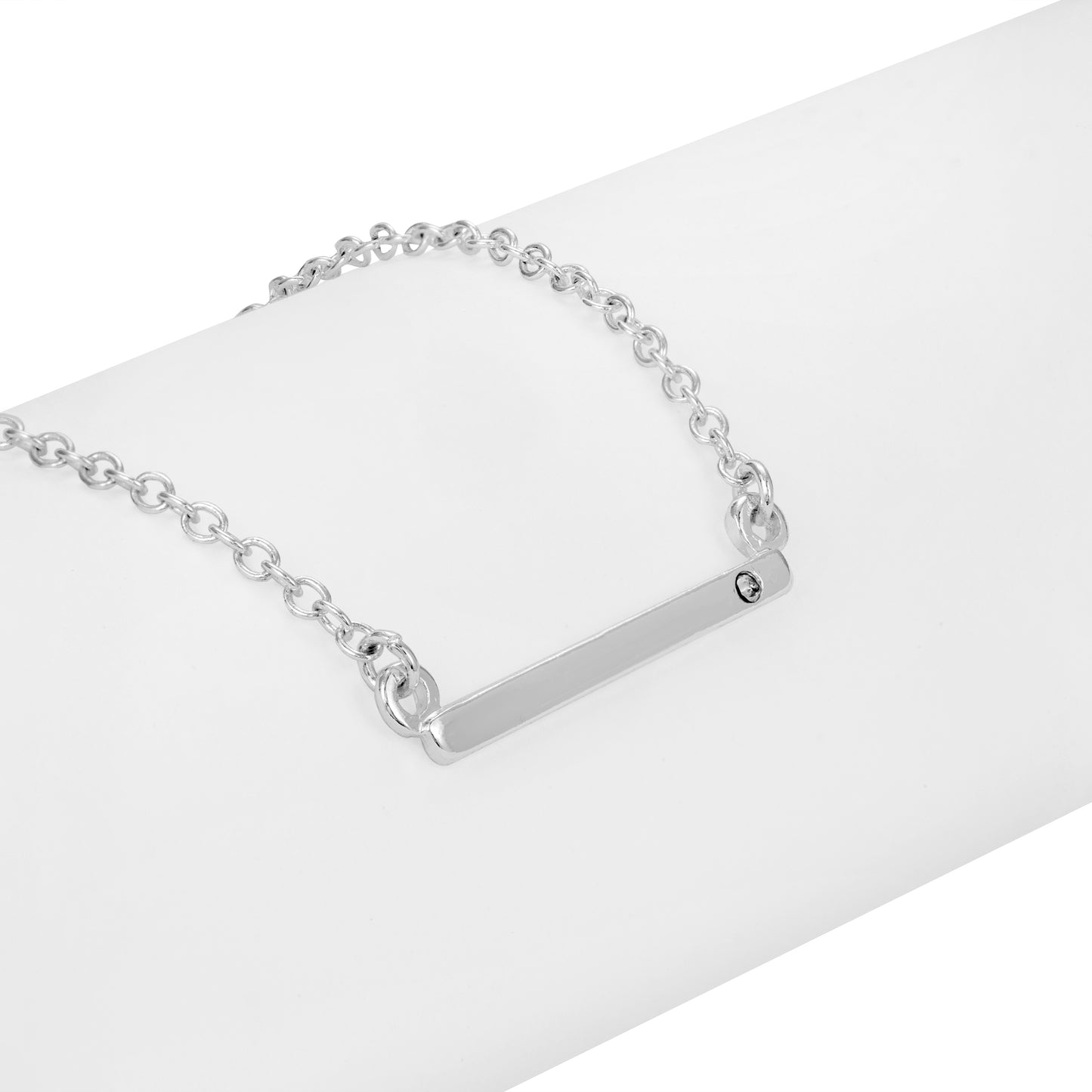 A silver chain necklace with a blank horizontal bar pendant rests on a white surface.