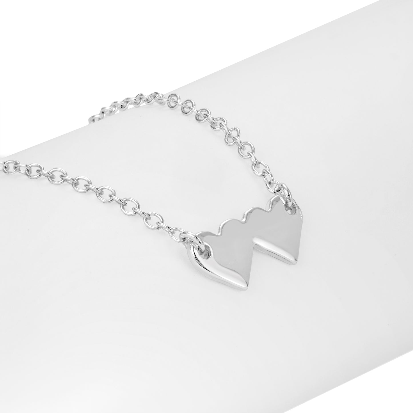 A silver-colored chain necklace with two heart charms rests on a white surface.