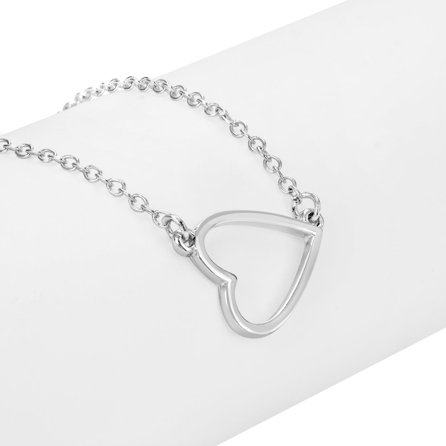 A silver heart pendant necklace rests on a white surface.