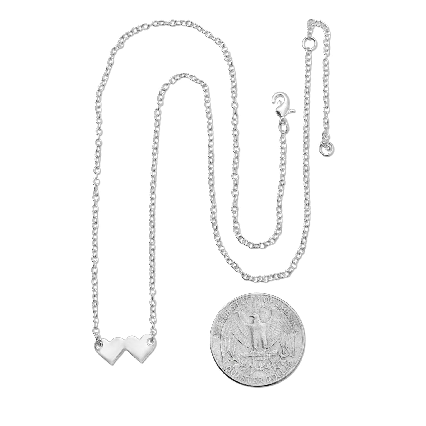 A silver-colored necklace with two adjacent heart pendants is shown next to a U.S. quarter for scale.