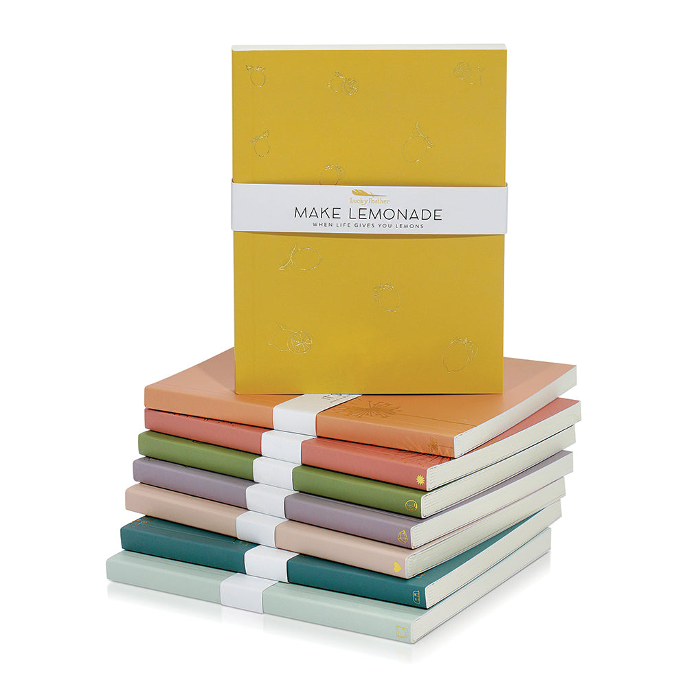 A stack of colorful journals, the top one bearing the words 'Make Lemonade.'