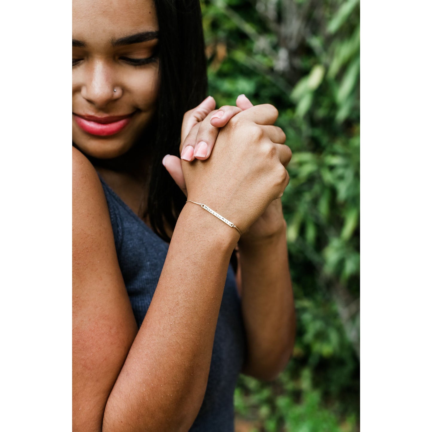 A smiling person clasps their hands, showing a delicate bracelet.