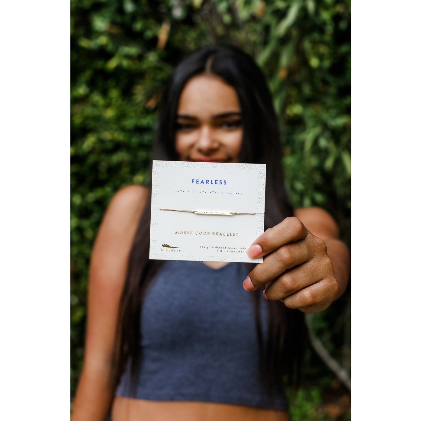 A person holds up a card displaying a "Fearless" morse code bracelet.