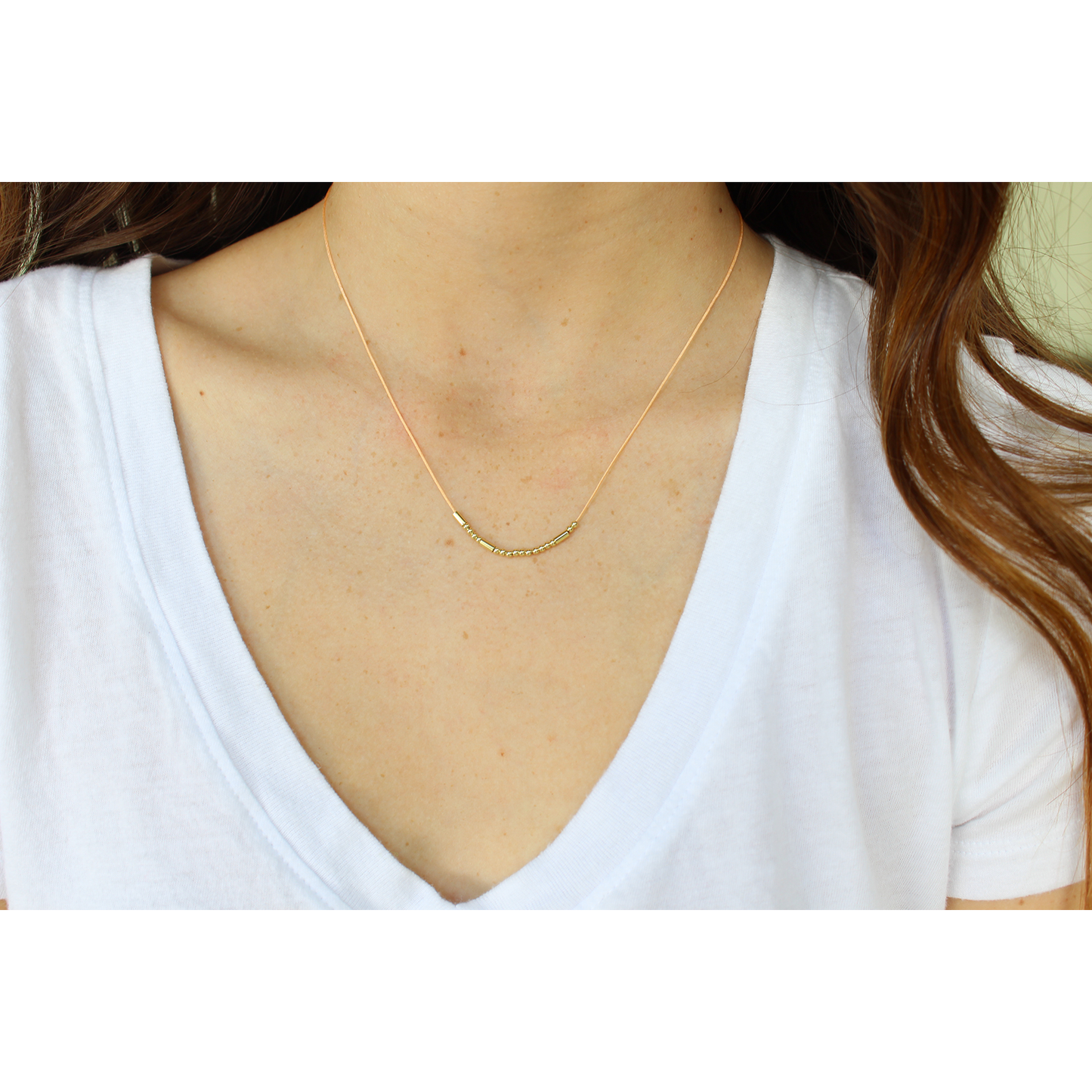 A person wearing a white v-neck shirt and a gold beaded necklace.