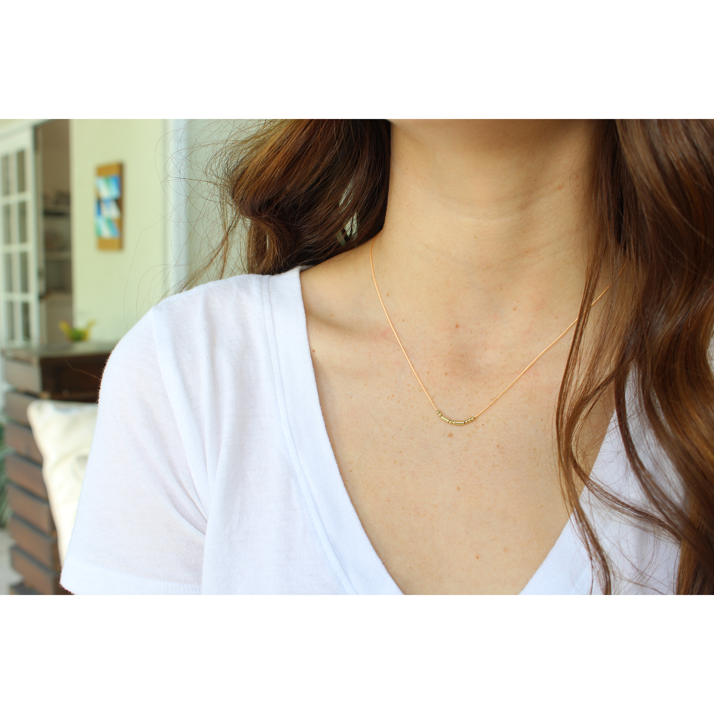 A person wears a simple beaded necklace and a white v-neck shirt.