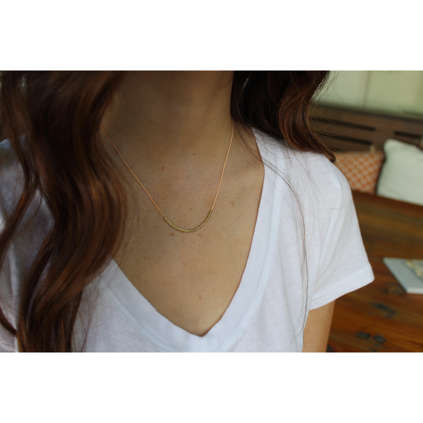 A person wearing a gold beaded necklace and a white v-neck shirt.