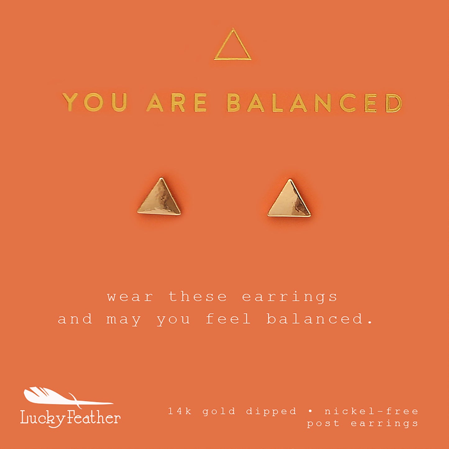 Two gold, triangular Lucky Feather post earrings on an orange card that reads "YOU ARE BALANCED."
