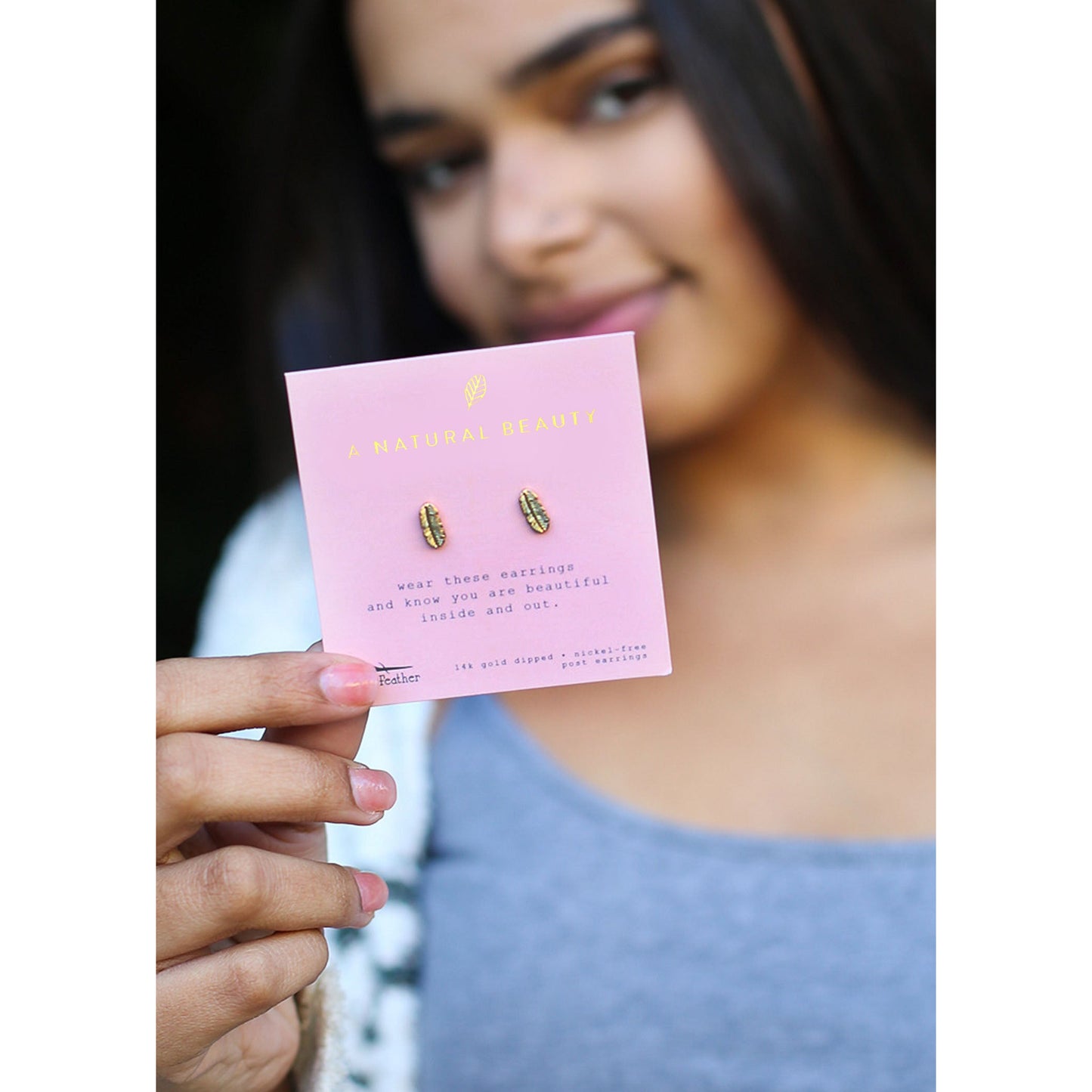 A woman holds up a card with gold feather earrings on it.