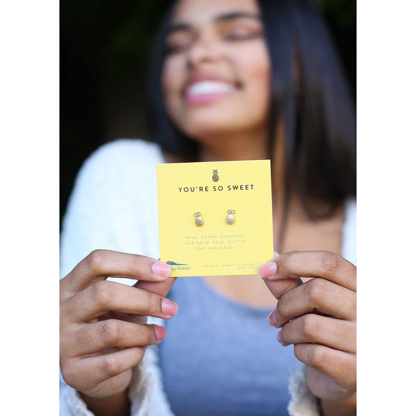 A smiling person holds a yellow card with pineapple earrings and the text "You're So Sweet."