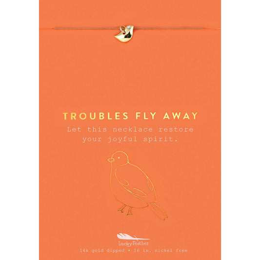 An orange card with a gold-colored bird charm, a gold-colored bird outline, and the words "Troubles Fly Away."