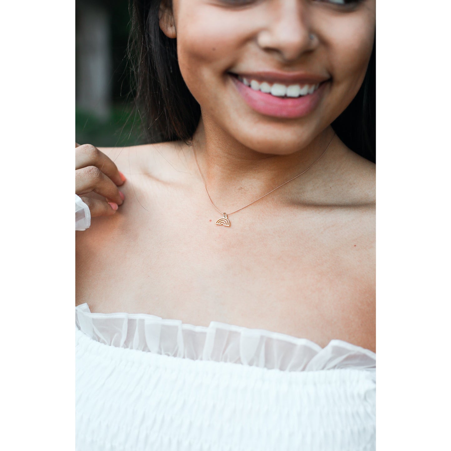 A smiling woman wears a gold rainbow necklace.