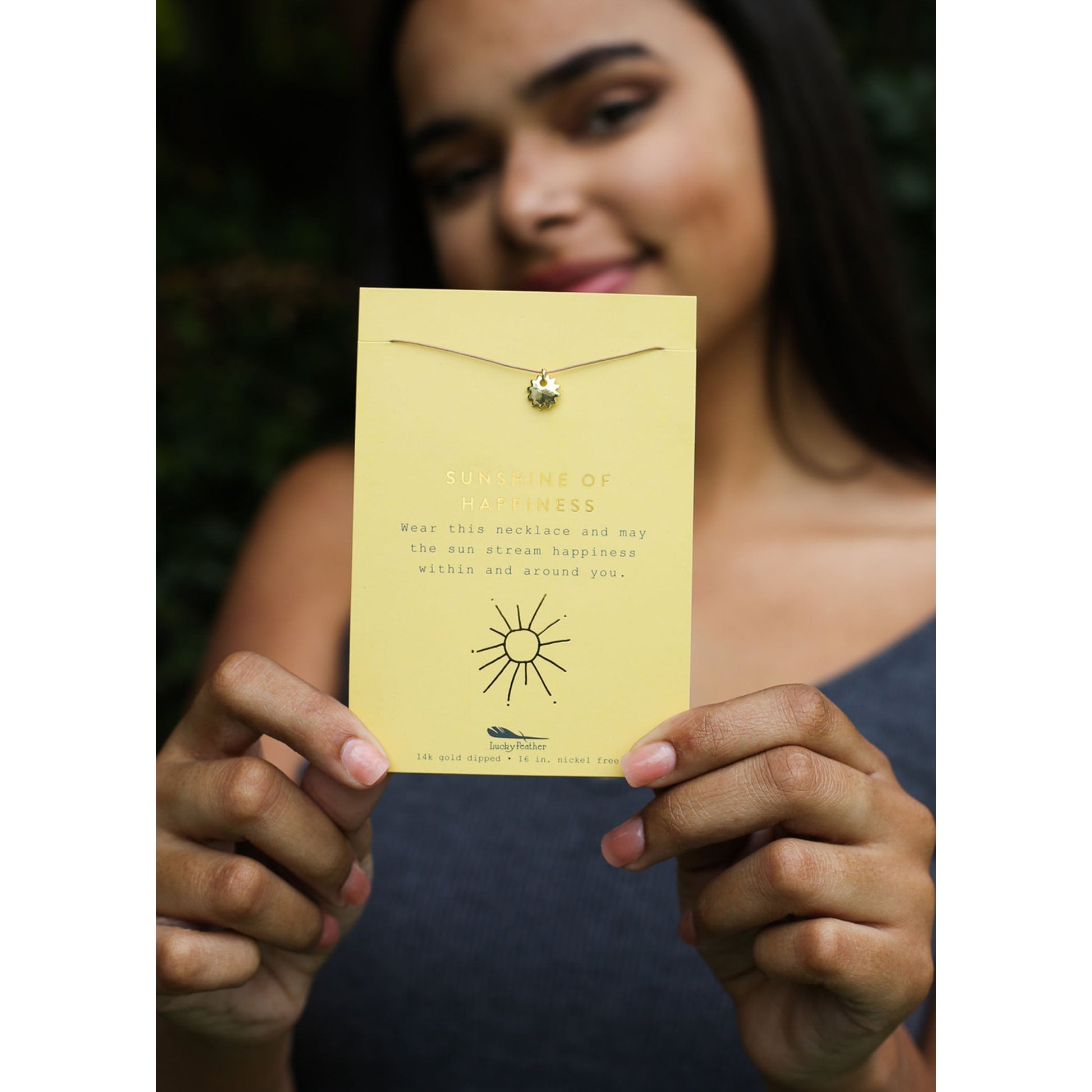 A person holds up a card displaying a necklace, the card reads "Sunshine of Happiness".