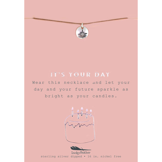 A necklace with a round pendant on a pink card that says "It's Your Day".