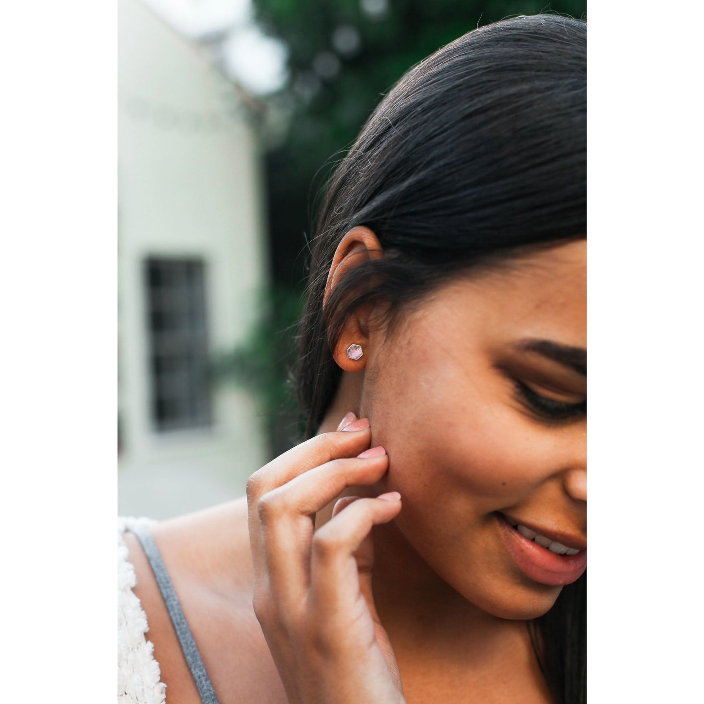 A woman with dark hair touches her face near a hexagon-shaped earring.