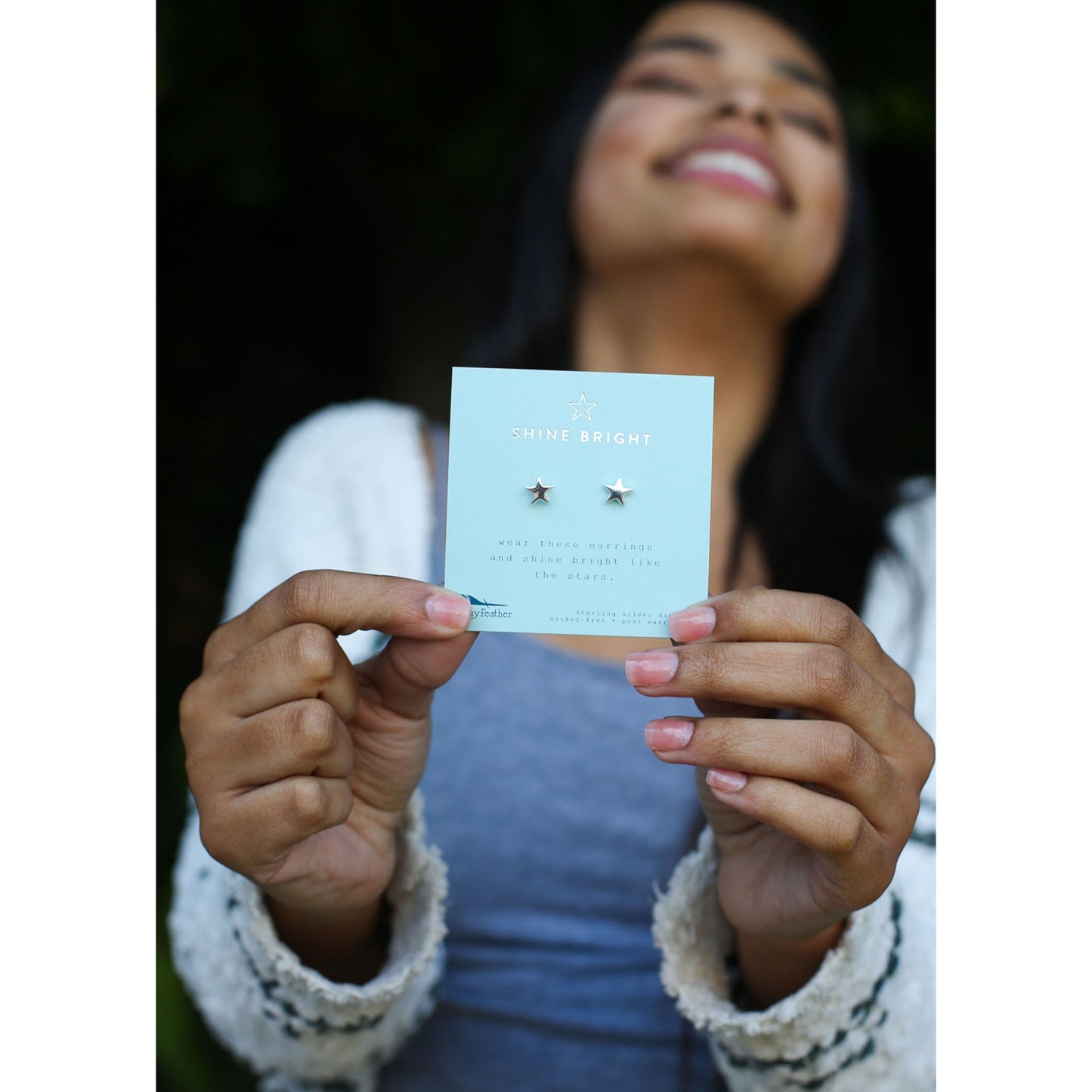 A smiling person holds a card with star-shaped earrings.
