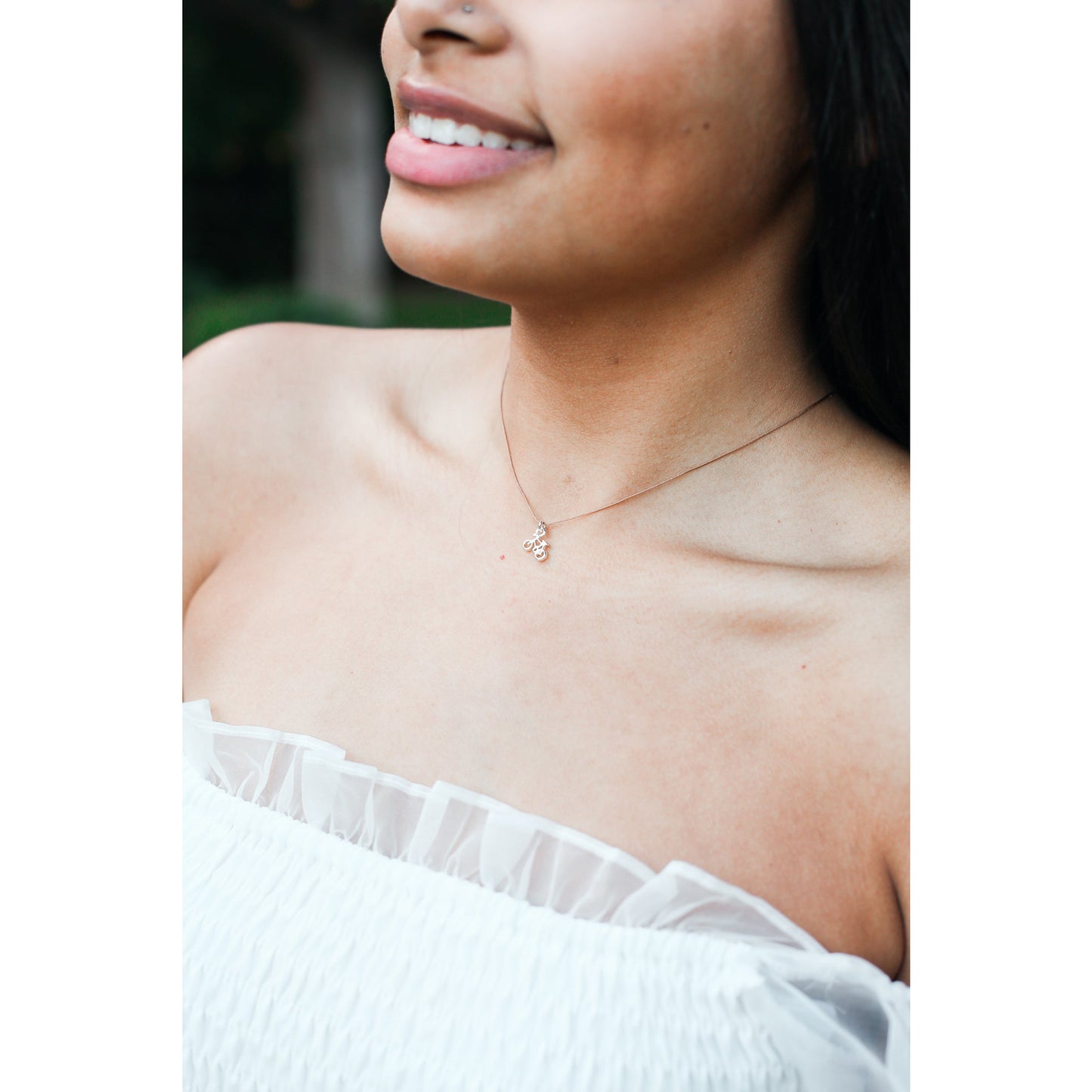 A person with a nose piercing wears a necklace and a white off-the-shoulder ruffled top.