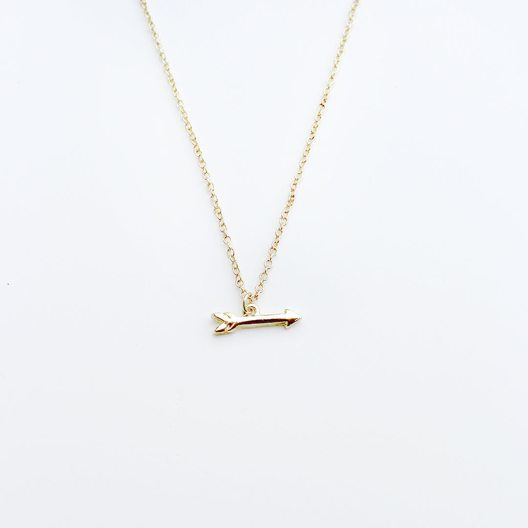 A gold necklace with an arrow pendant is displayed against a white background.