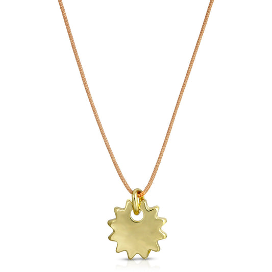 A gold sunburst pendant hangs from a tan cord necklace.