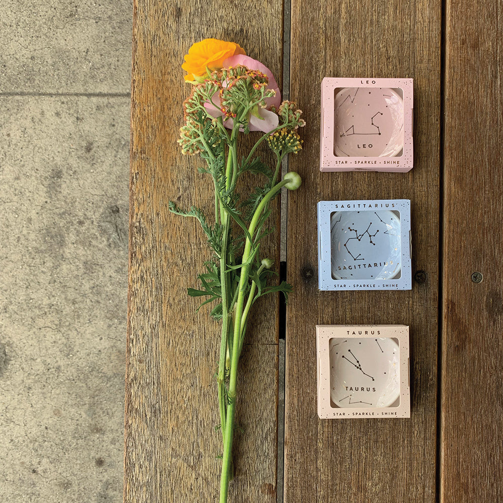 A ranunculus flower and three small boxes with zodiac signs are on a wooden surface.