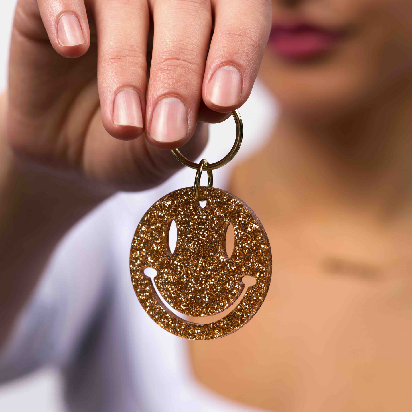 A hand holds a golden glittery smiley face keychain.